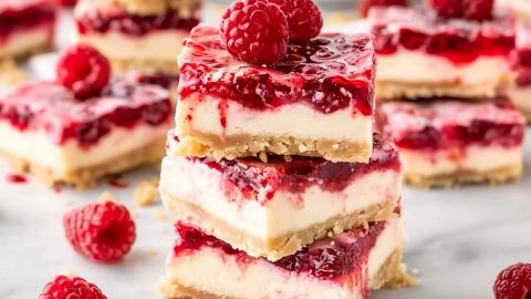 Homemade raspberry bars with vanilla cheesecake layer and graham cracker crust on a parchment paper in a white marble table