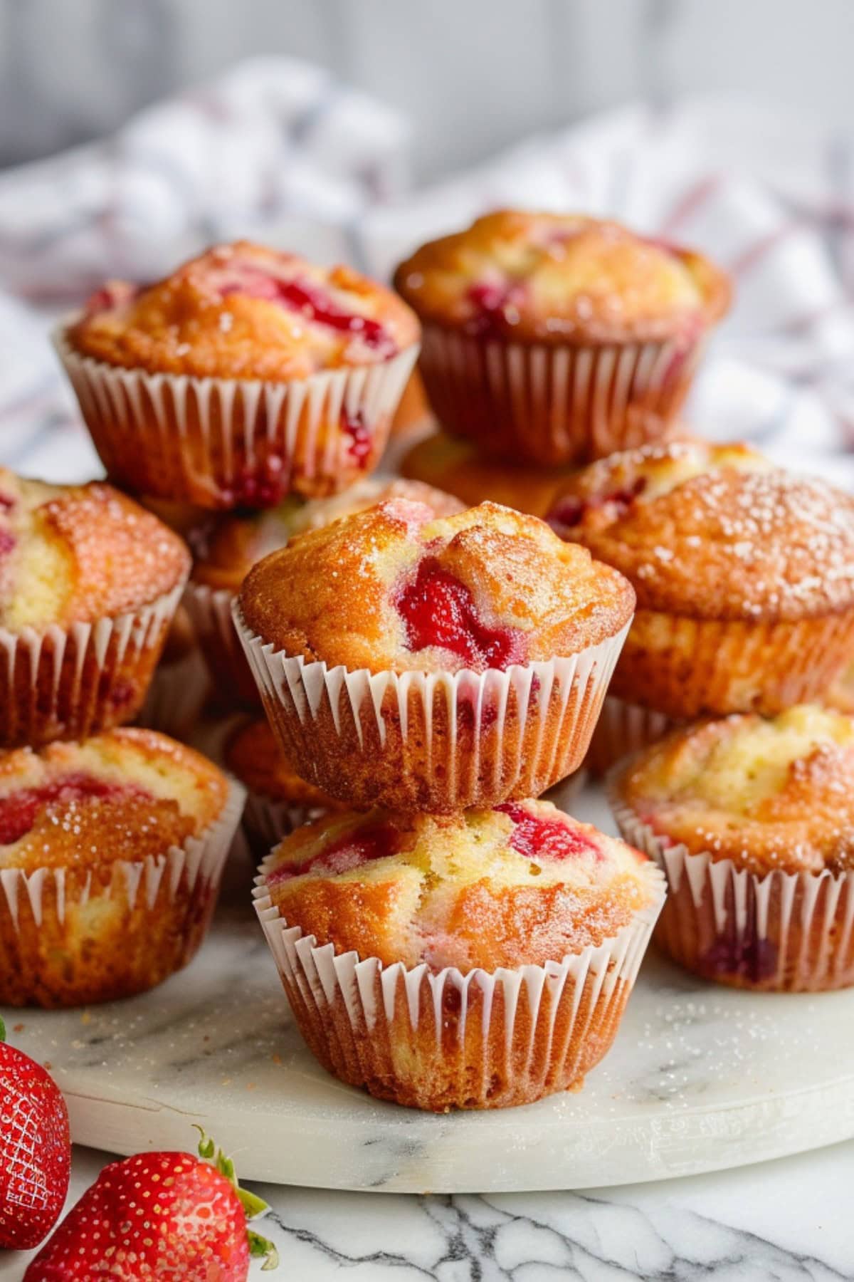 Stacked strawberry muffins on a marble platter topped with turbinado sugar
