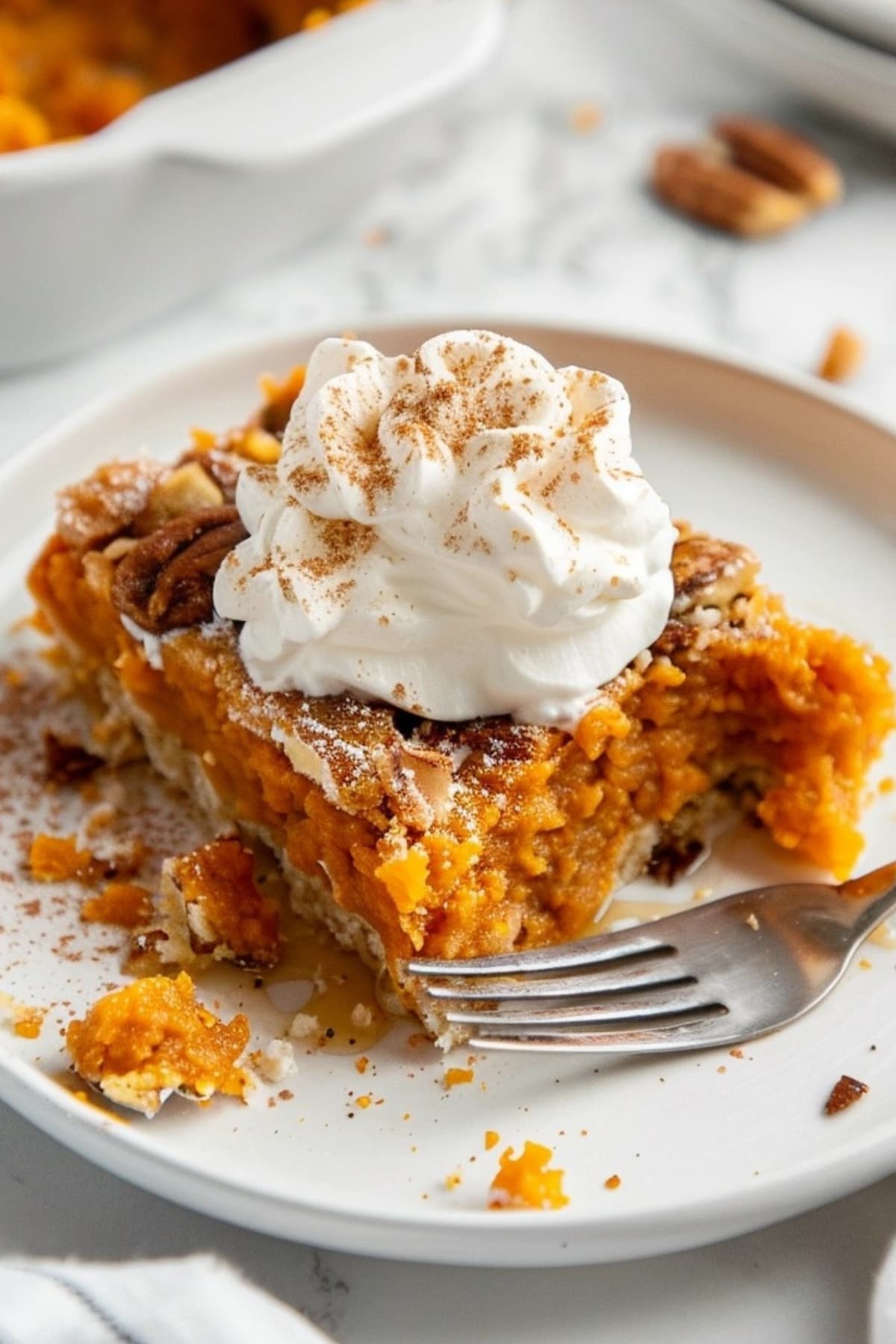 Sweet potato dump cake in white plate topped with whipped cream, fork on the side.