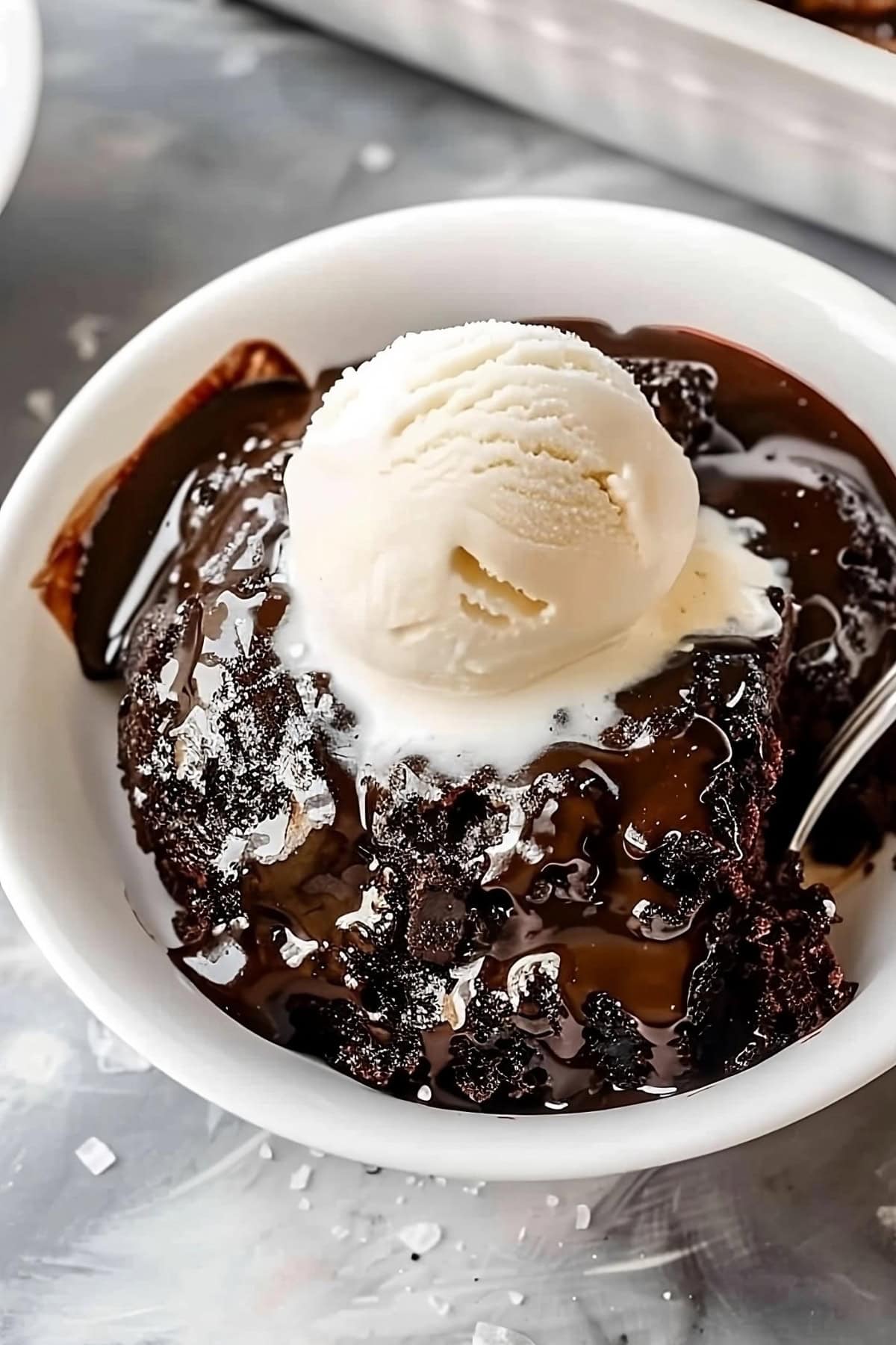 Top view of a serving of hot fudge cake in a white bowl with ice cream.