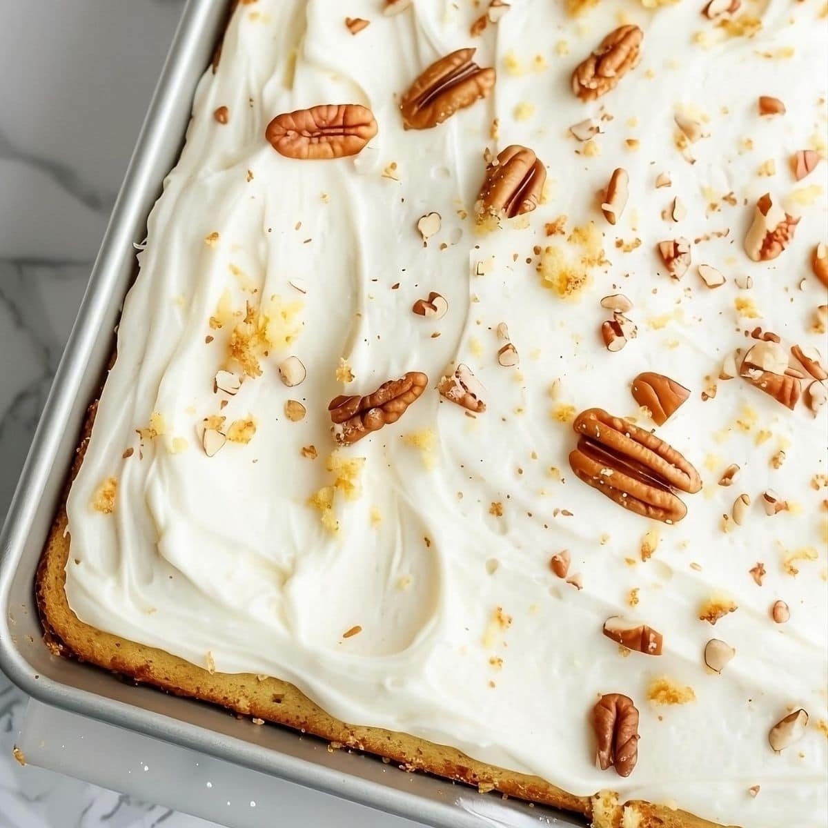 Top down view of a pineapple sheet cake with cream cheese frosting and chopped pecans