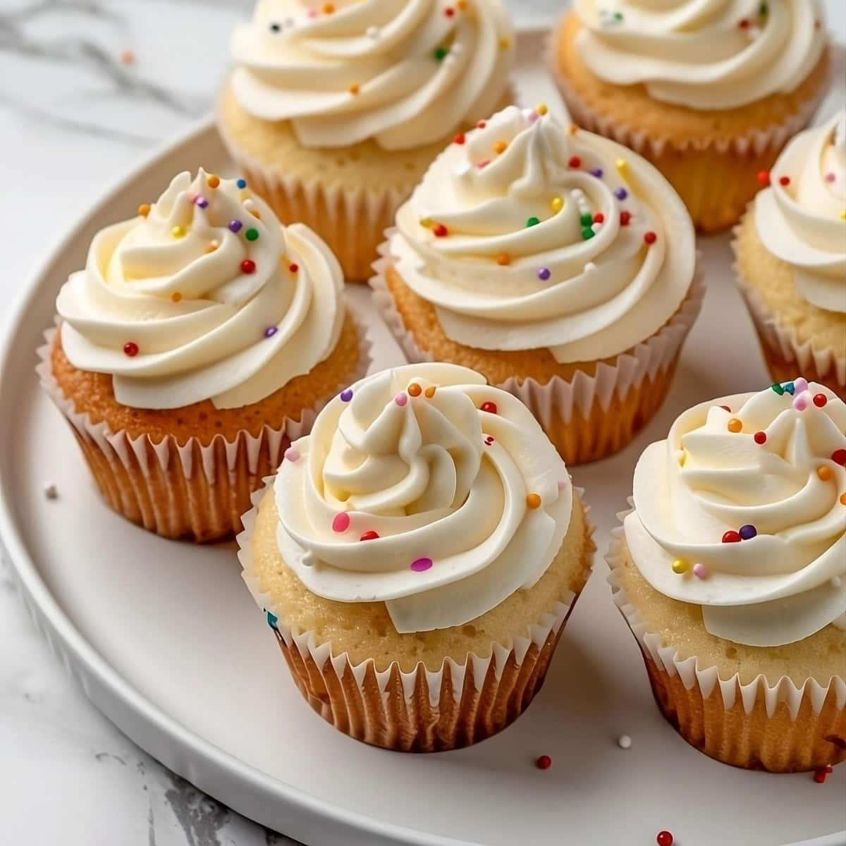 Vanilla cupcake with frosting garnished with sprinkles arranged in a plate.