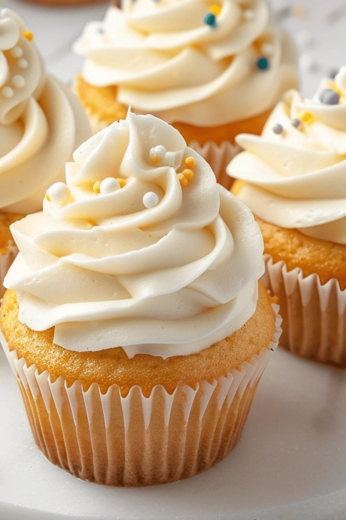 Closeup of vanilla cupcakes topped with smooth buttercream frosting and sprinkles.