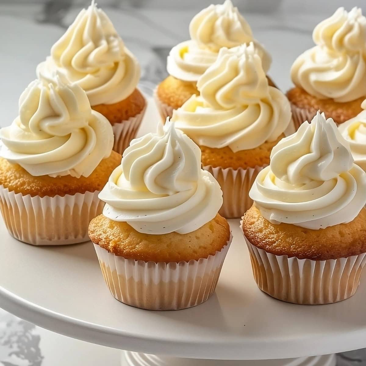 Vanilla cupcakes with buttercream frosting arranged in a cake tray.