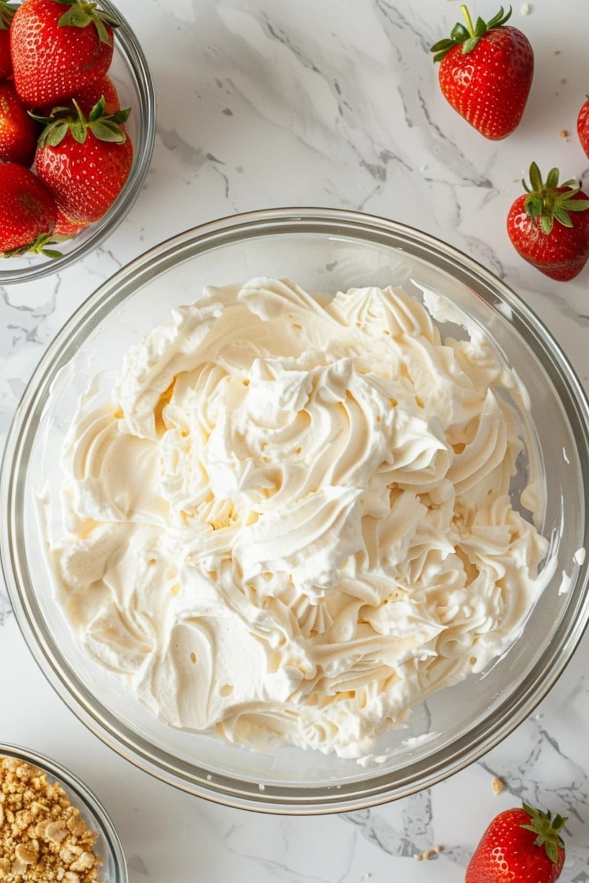 Whipped cream in a glass bowl with fresh strawberries and crush graham crackers on the side, top down view.