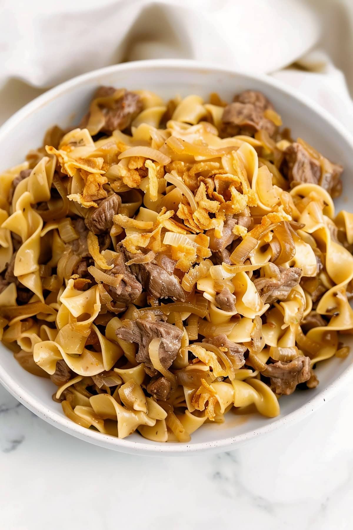 Comforting beef and egg noodles with onions in a white bowl
