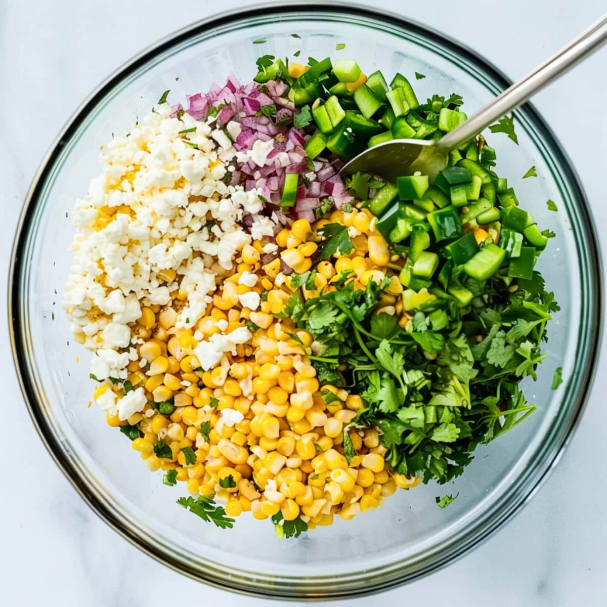 Corn, cilantro, chopped jalapeno, chopped red onions, and crumbled cheese in a glass bowl.