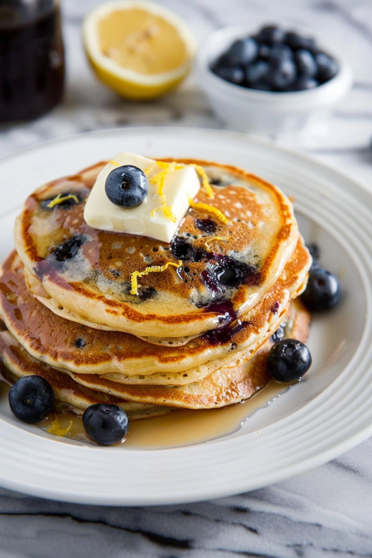 Delicious lemon blueberry pancakes, paired with a side of fresh fruits and topped with butter and lemon zest.