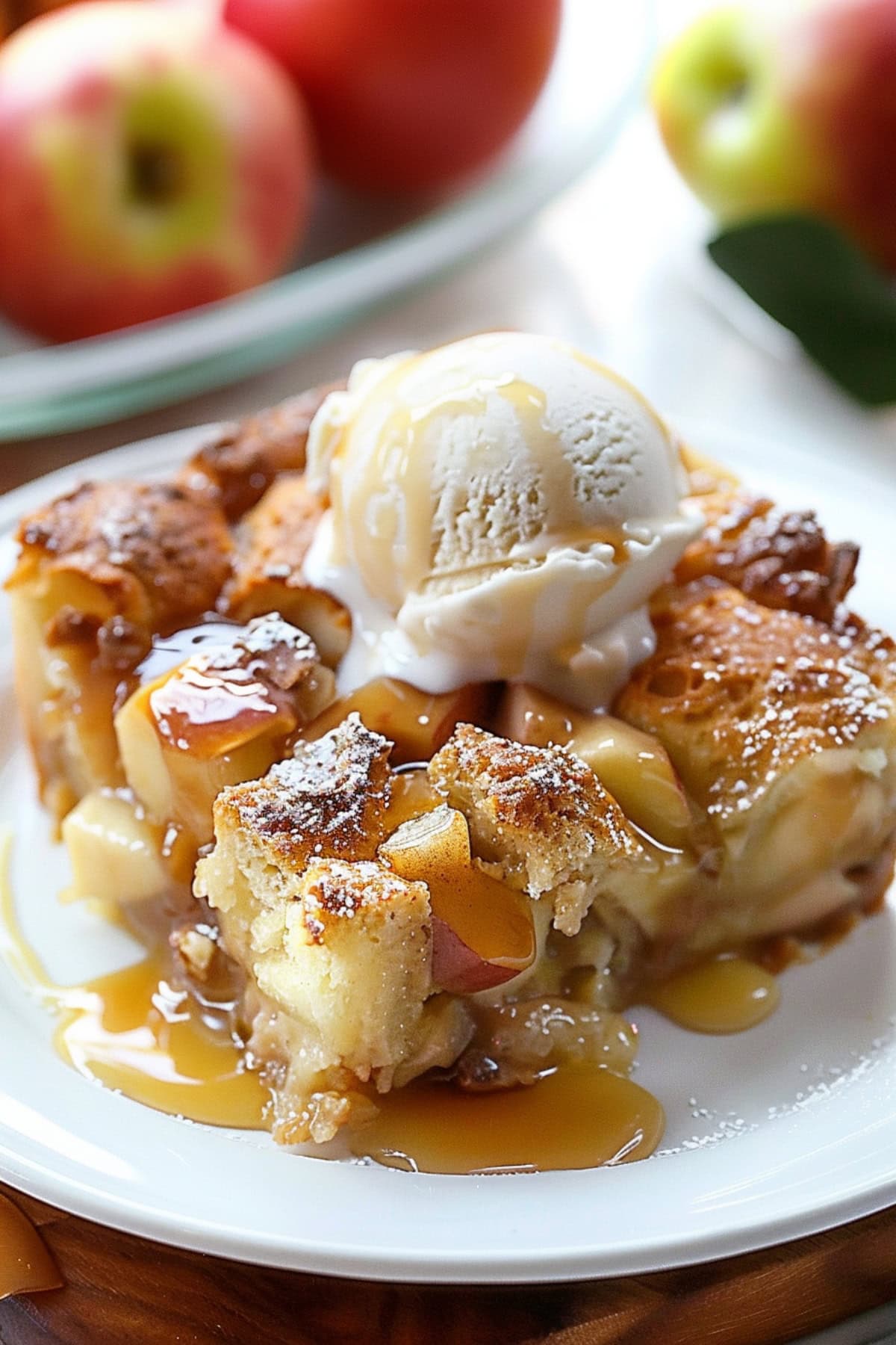 Apple pie bread pudding topped with vanilla ice cream and caramel sauce on a white table.