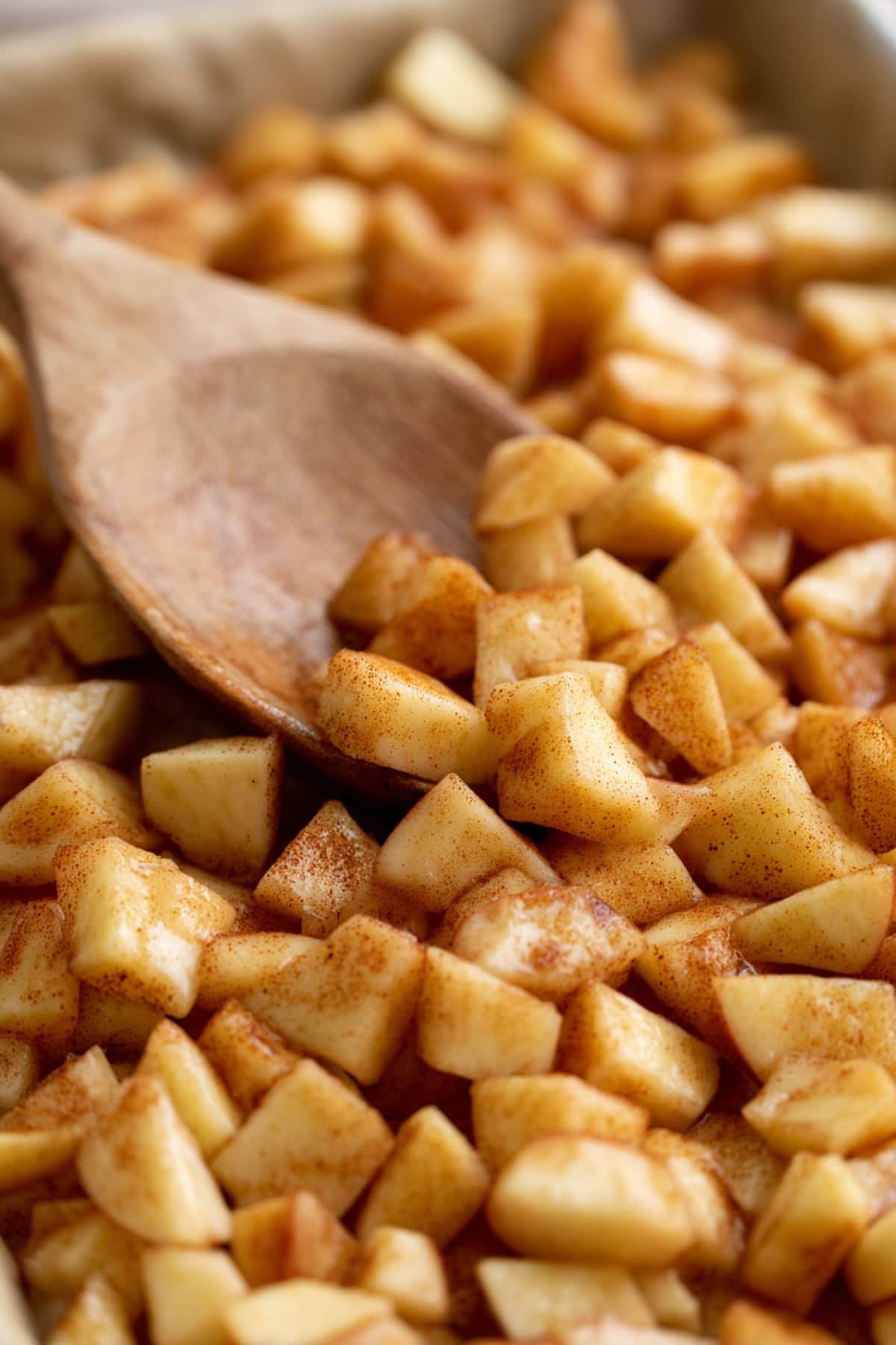 Close-up of chopped apples coated with cinnamon and sugar, stirred with a wooden spoon.