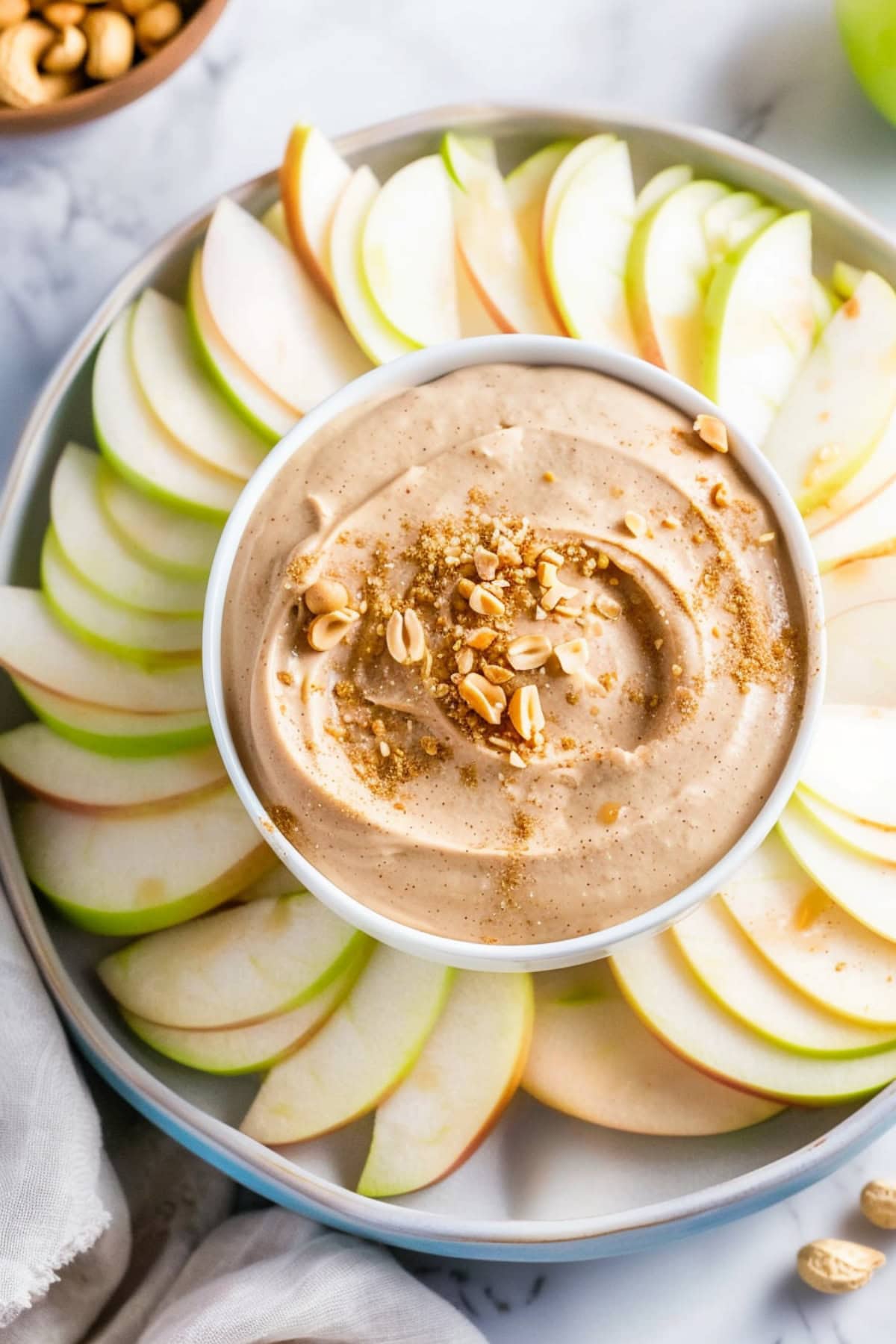 Thinly sliced green apples with creamy peanut butter dip in bowl.
