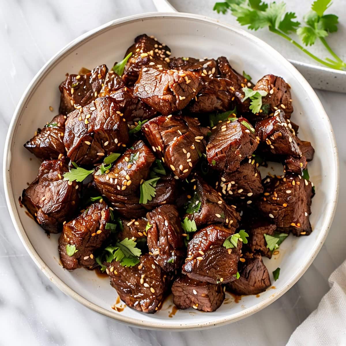 Asian steak bites marinated with sweet and savory sauce, garnished with green cilantro and toasted sesame seeds