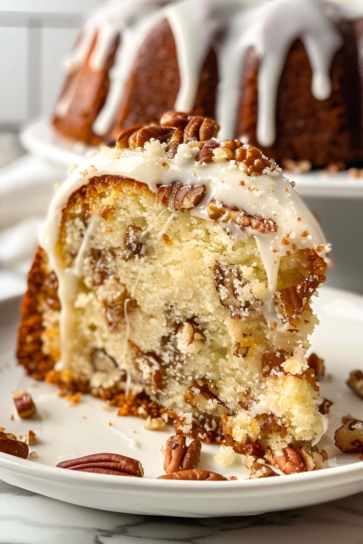 Close Up of Slice of Bacardi Rum Cake with Pecans and a Rum Glaze, Topping With More Nuts and the Rest of the Cake on a Cake Stand in the Background