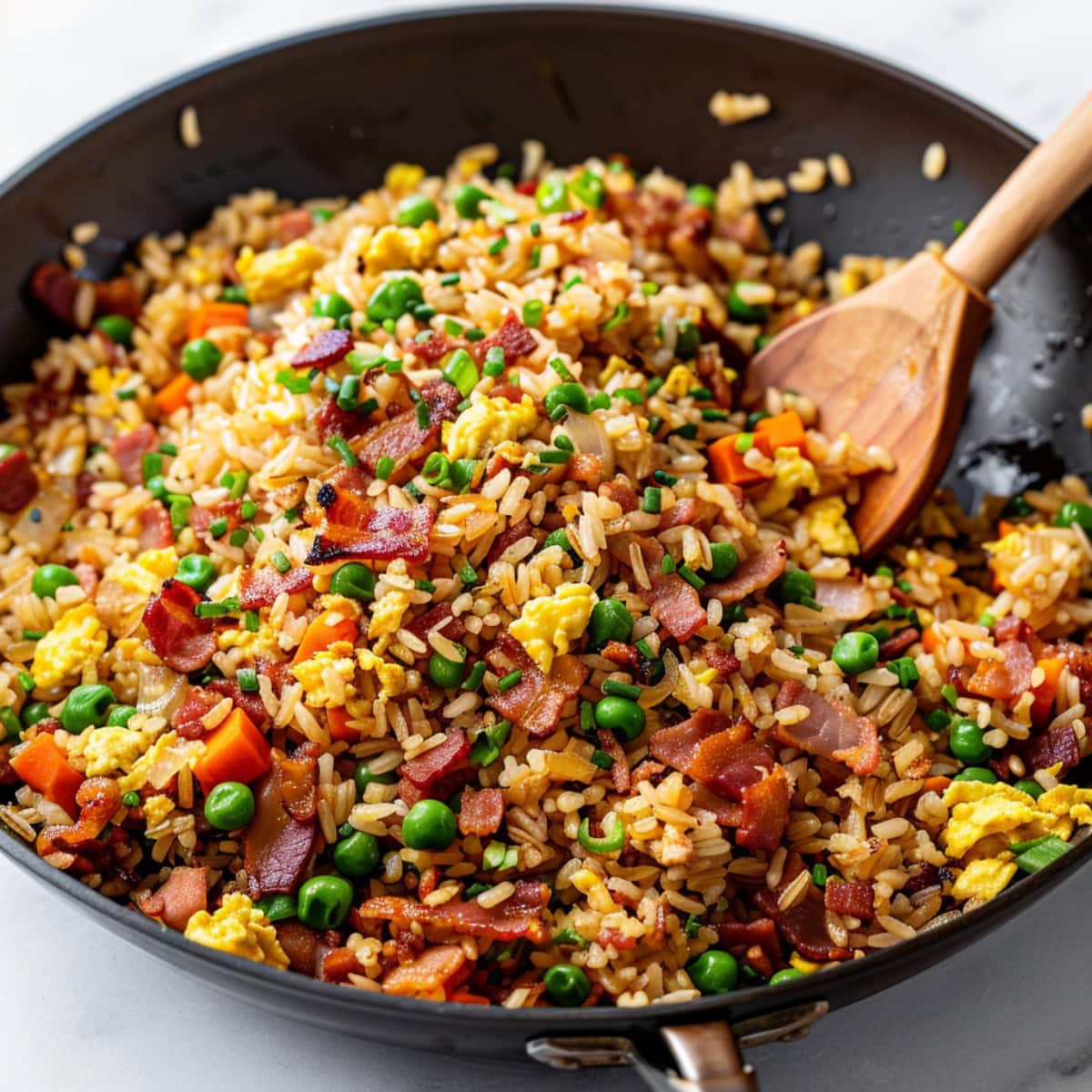 Bacon fried rice tossed in a skillet pan with a wooden ladle.