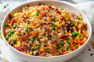 Bowl of fried rice with bacon, egg, green peas and carrots.