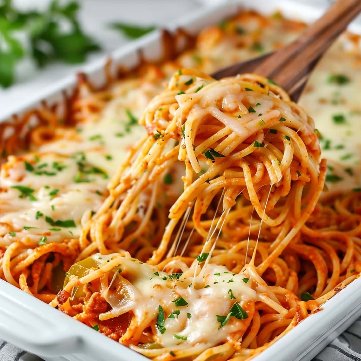 Wooden ladle lifting baked cream cheese spaghetti from a baking dish.