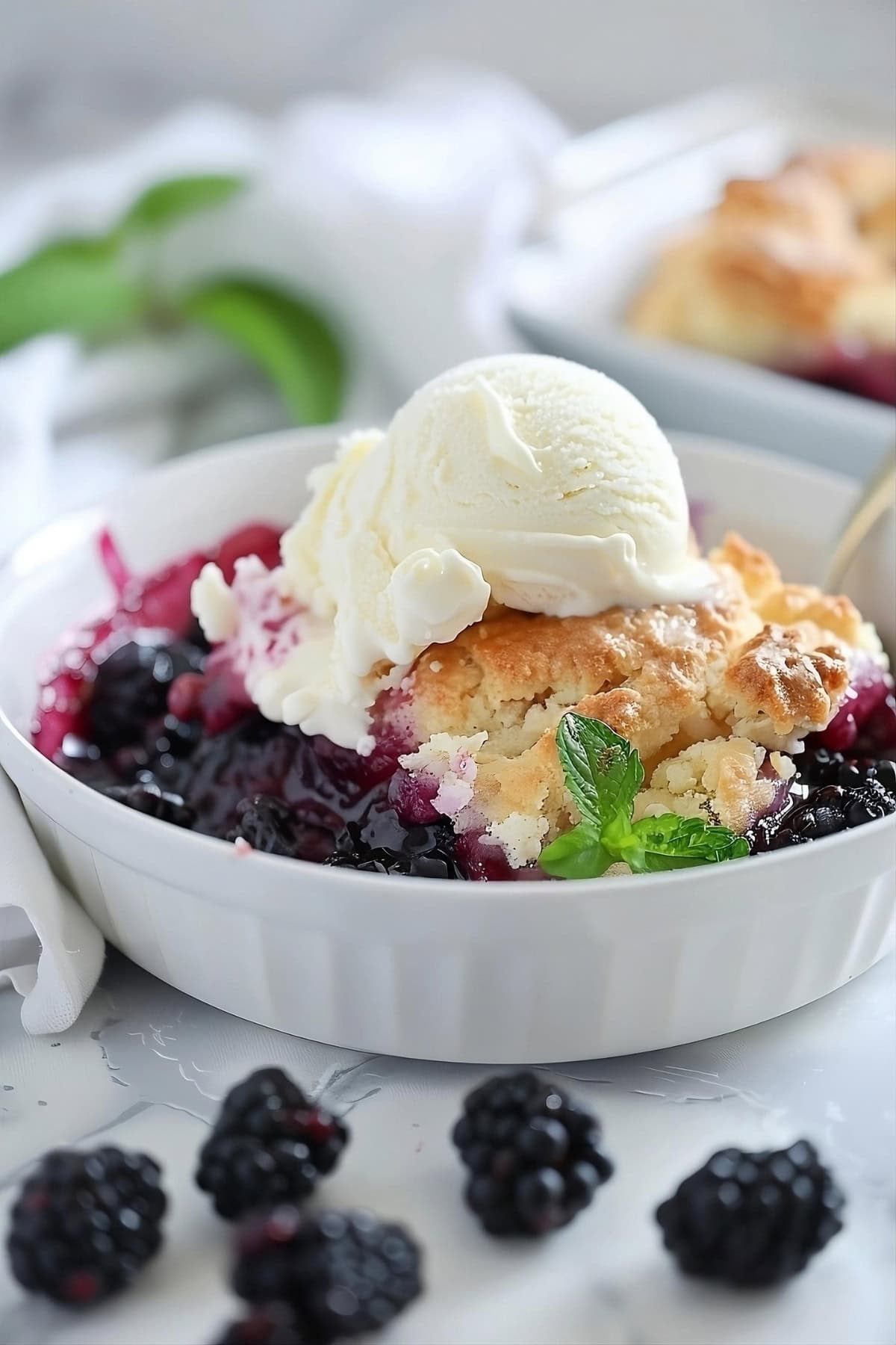Blackberry cobbler served in a white bowl topped with scoop of vanilla ice cream.
