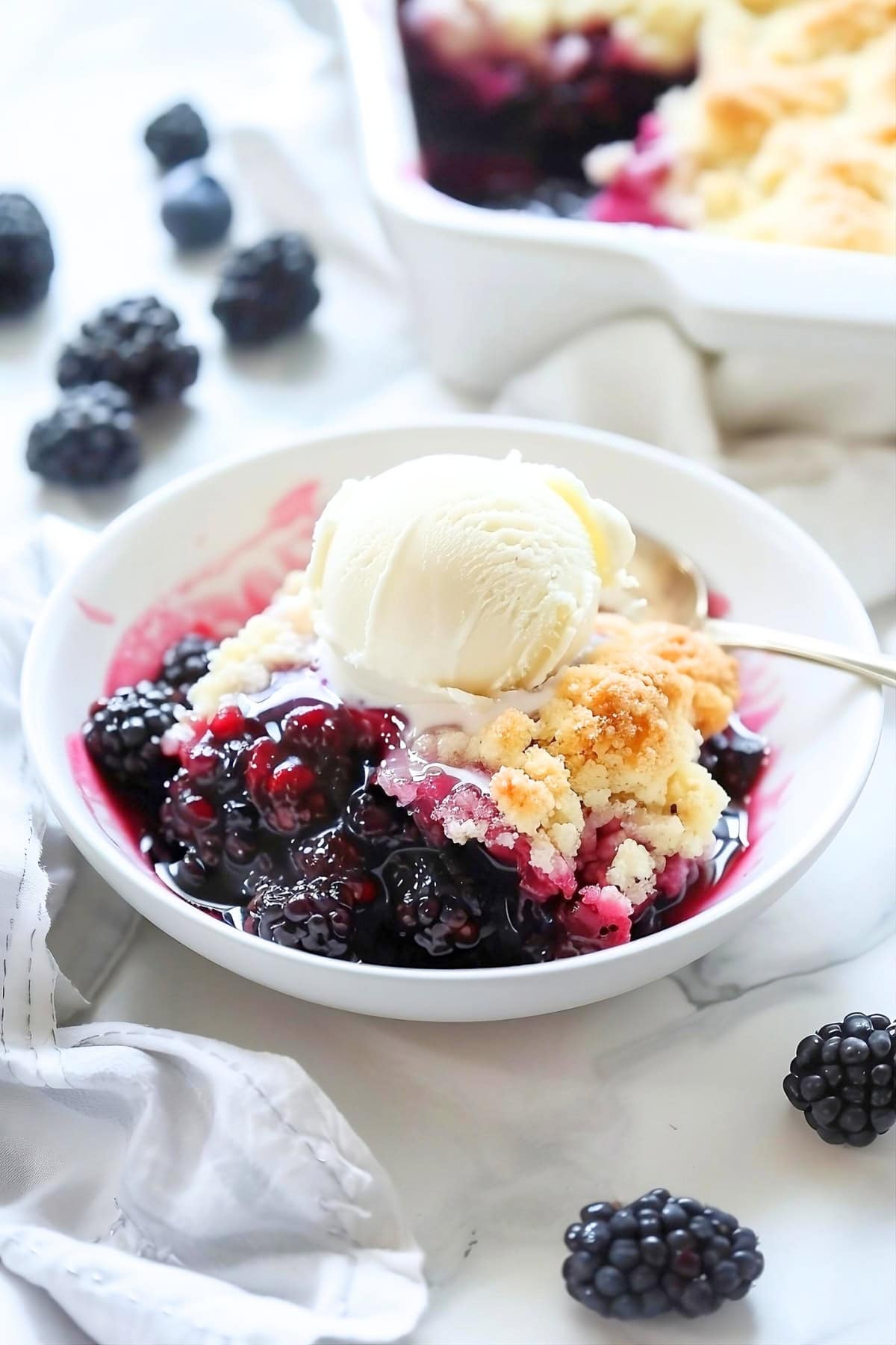 Serving of blackberry cobbler in a white bowl with a scoop of vanilla ice cream.