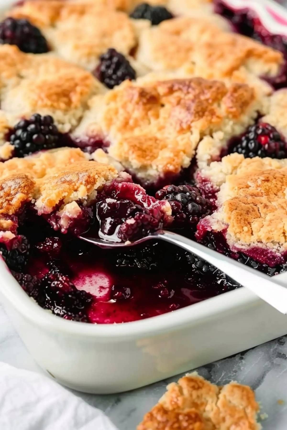 Blackberry cobbler scooped with a spoon in a baking dish.