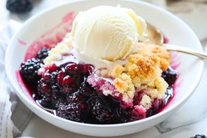 Blackberry cobbler in a white bowl garnished with vanilla ice cream on top.