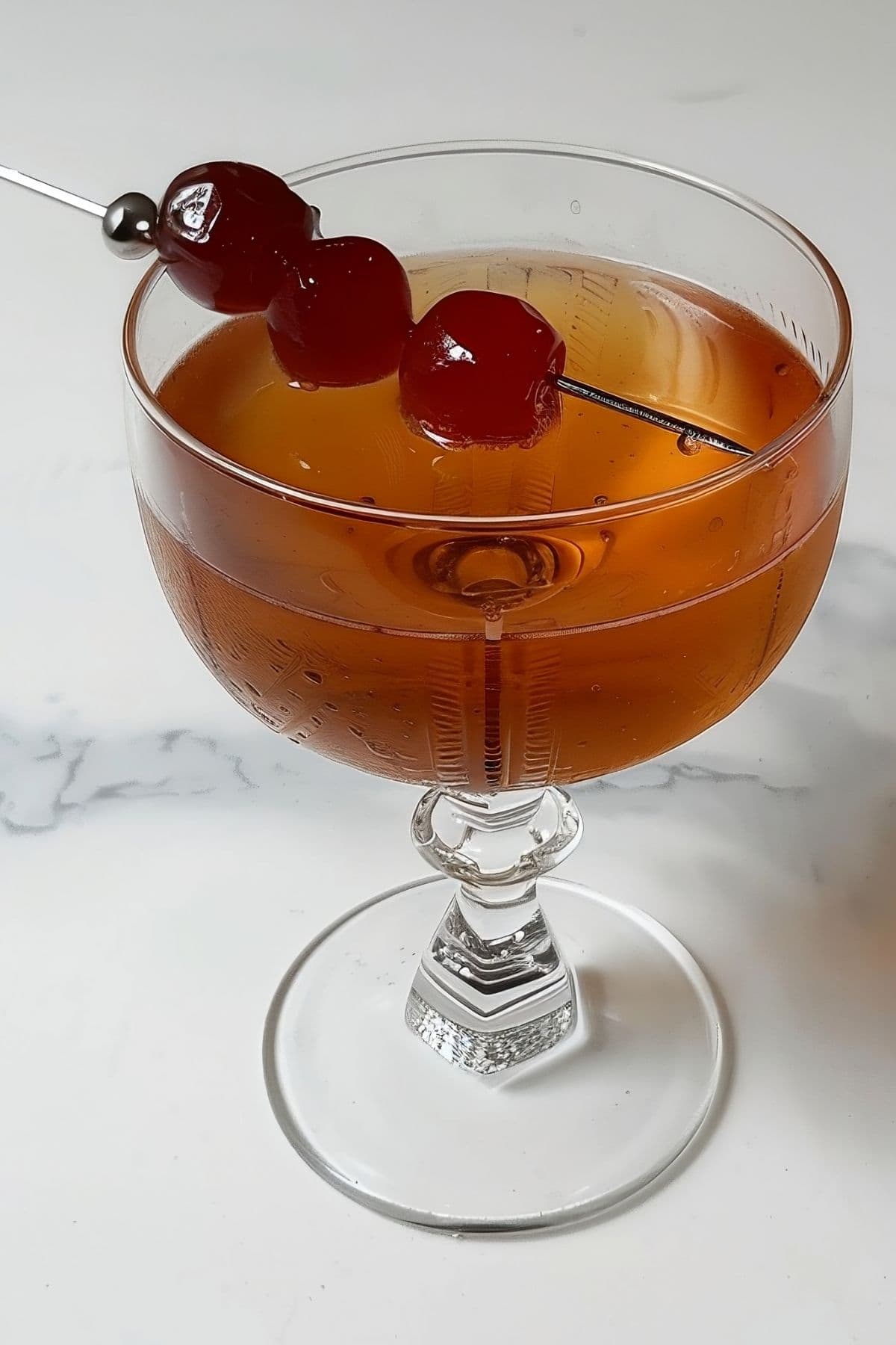 Close Side Top View of Brooklyn Cocktail in a Coupe Glass with Three Luxardo Maraschino Cherries on a Metal Skewer for Garnish