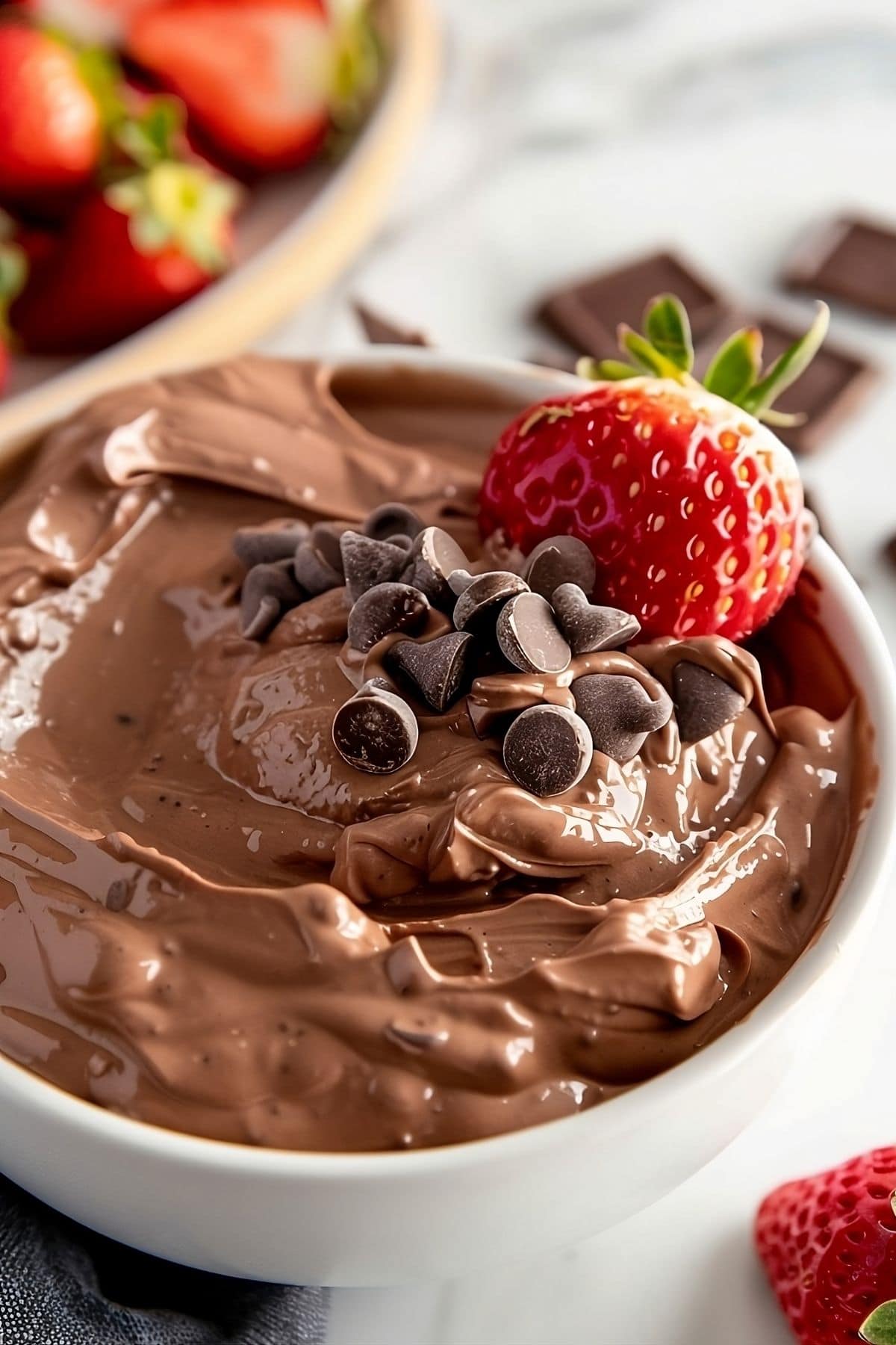 Chocolate brownie batter dip in a white bowl garnished with fresh strawberries and mini chocolate chips. 