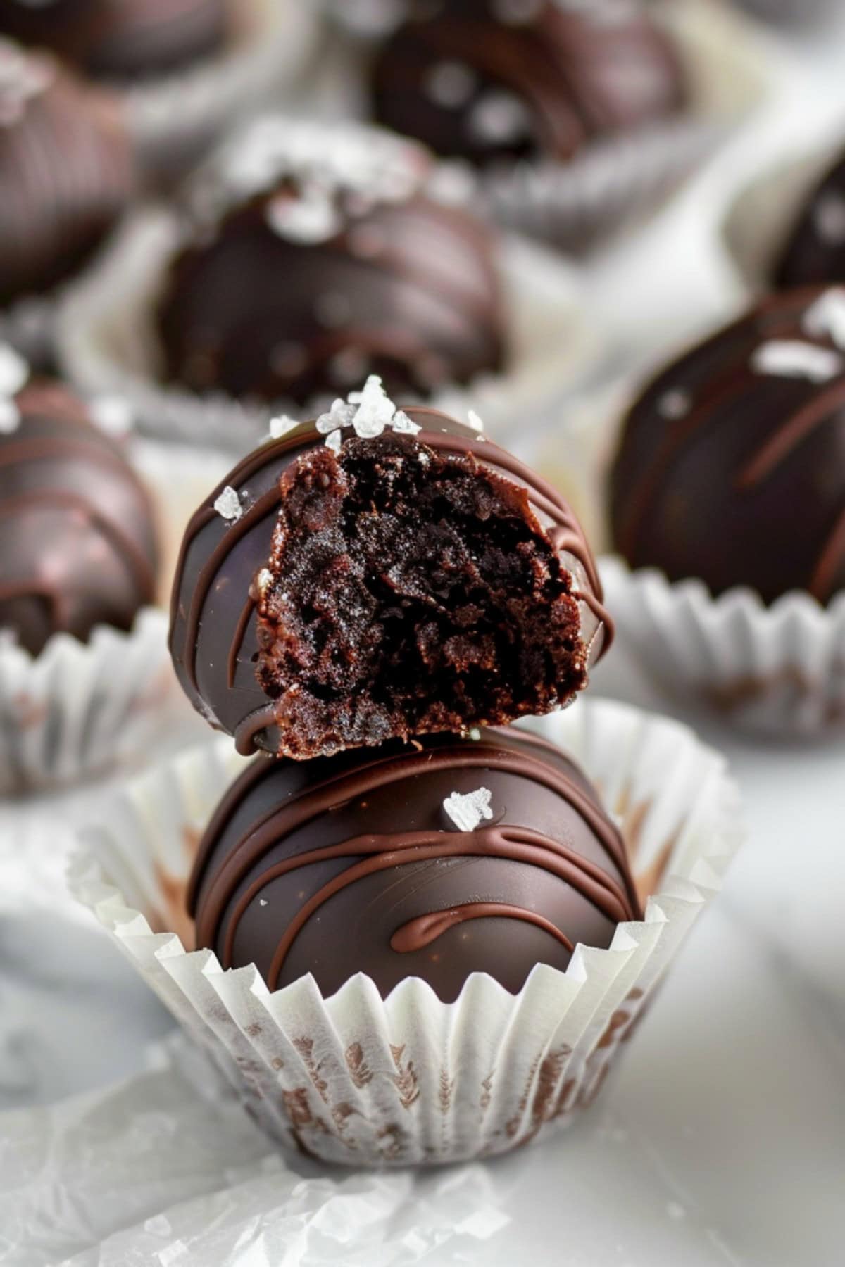 Decadent and fudgy homemade brownie truffles topped with sea salt placed in paper cups on a white marble countertop