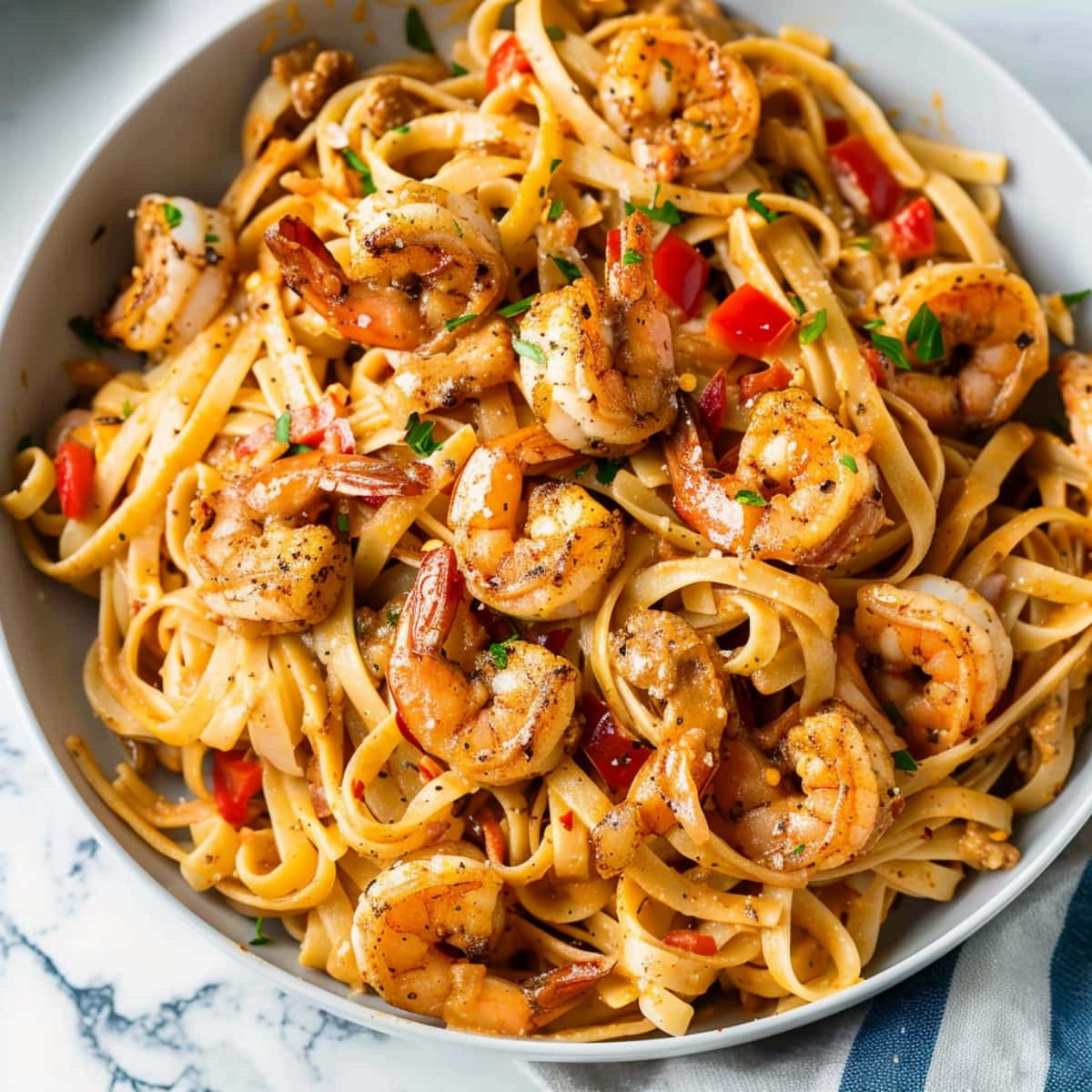 A white bowl of Cajun shrimp pasta with chopped bell peppers and parsley