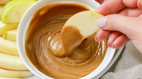 A bowl of rich, creamy caramel dip surrounded by fresh apple slices