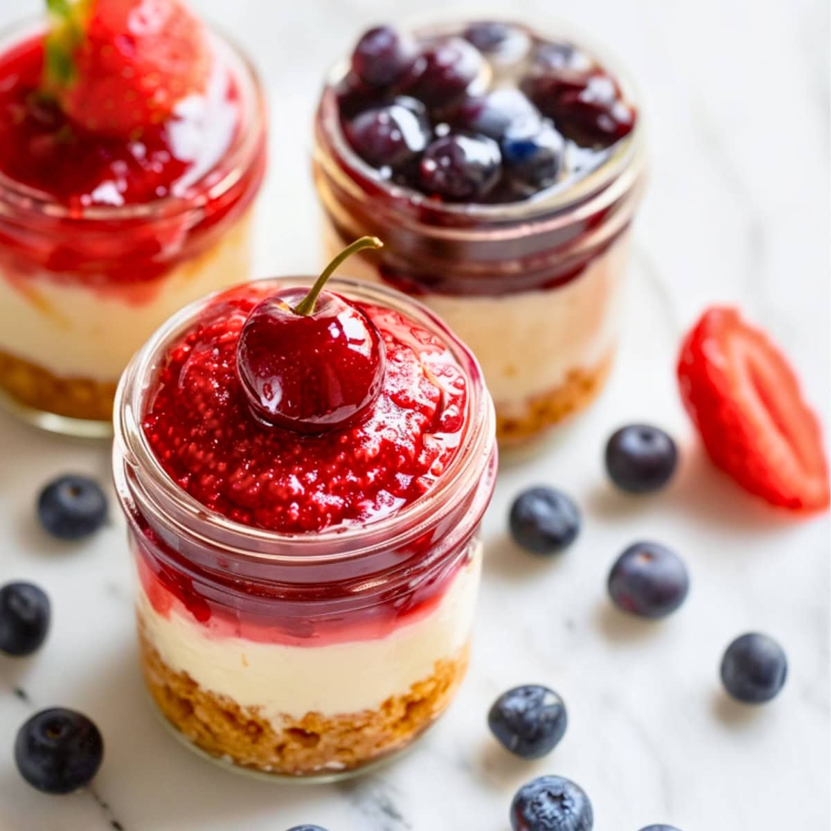 Three cheesecake jar with strawberry, blueberry and cherry on top.