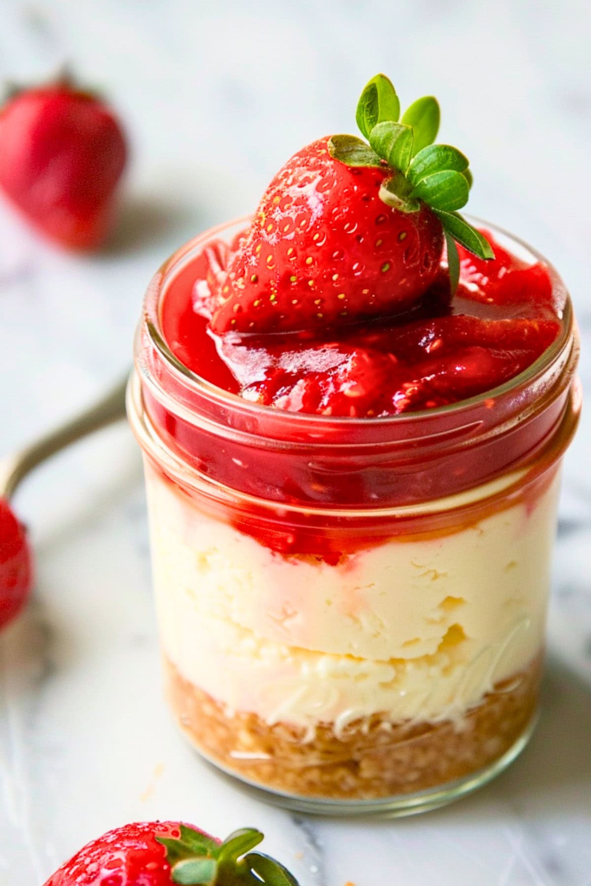 Close-up shot of a jar of cheesecake with fresh strawberry on top.