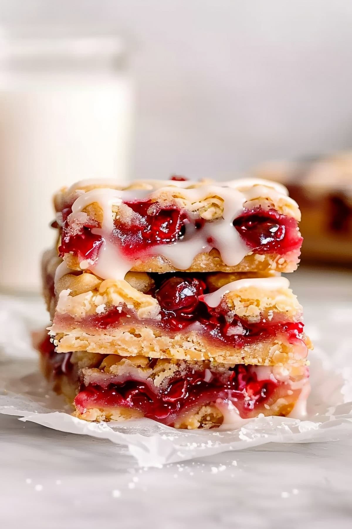 Homemade cherry pie bars with vanilla glaze stacked on top of each other on a white parchment paper