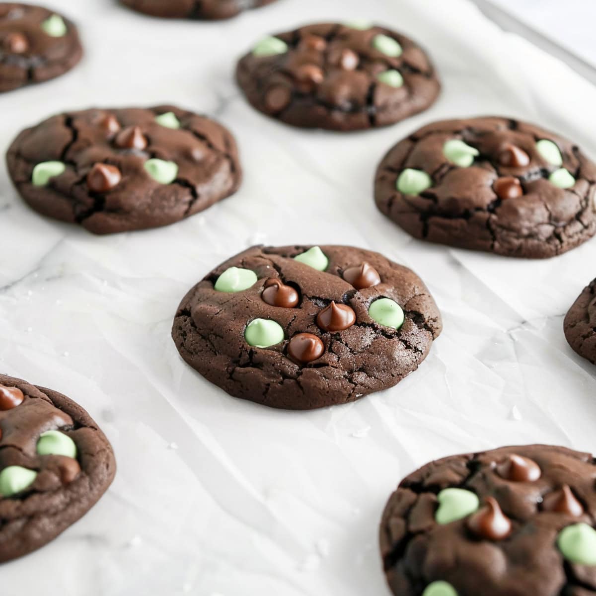 A close-up shot of freshly baked chocolate mint chip cookies on a white parchment paper.