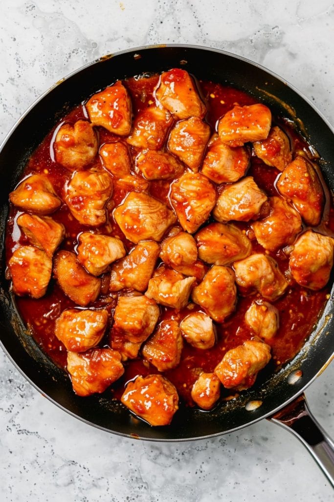 Chicken bites with spicy sauce in a black skillet, overhead view