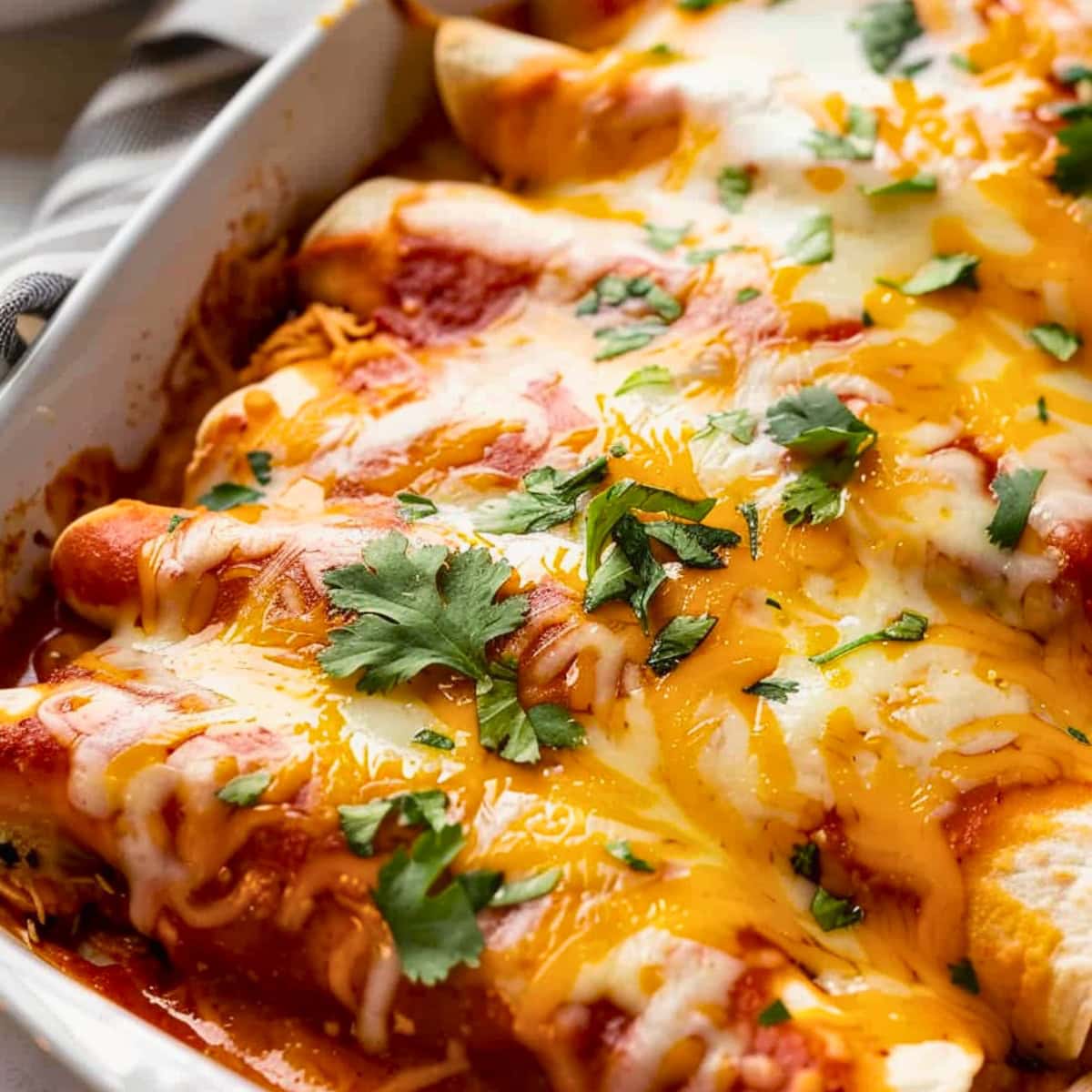 Cheesy chicken enchilada in baking dish garnished with cilantro leaves.