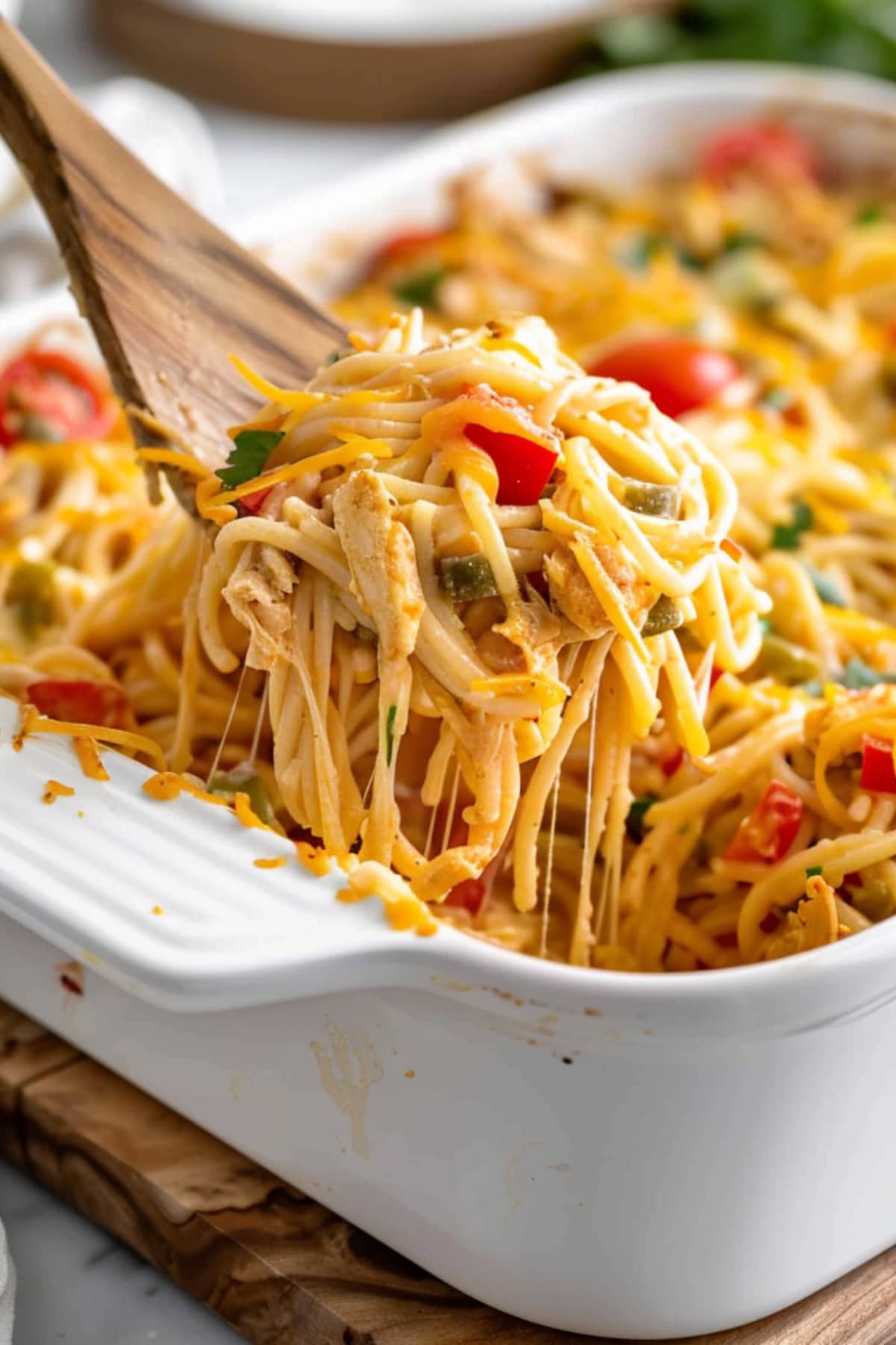Cheesy chicken spaghetti casserole lifted by a wooden ladle.