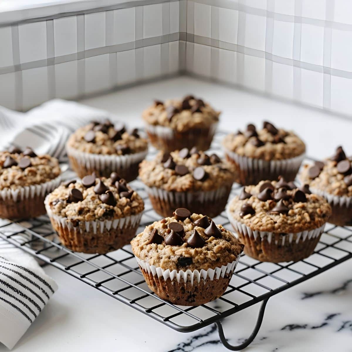 Chocolate Chip Oatmeal Muffins in Liners Cooling on a Wire Rack on a White Marble Countertop