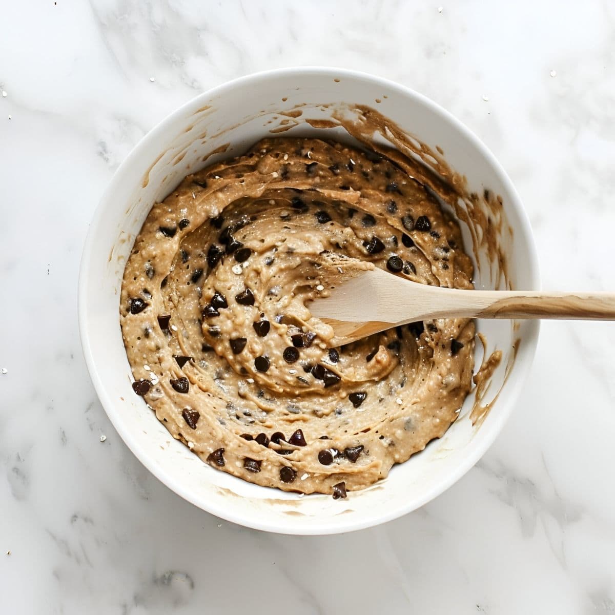 Chocolate Chip Oatmeal Muffin Batter in a White Bowl with a Wooden Spoon- Top View