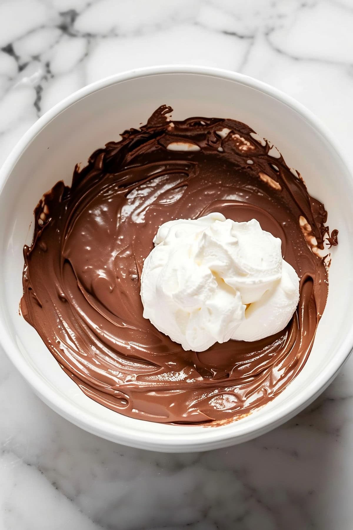 Melted chocolate and a dollop of heavy whipping cream in a white bowl