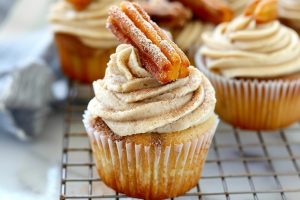 Cupcakes with cinnamon frosting garnished with a slice of churro arranged in a while cooling rack.