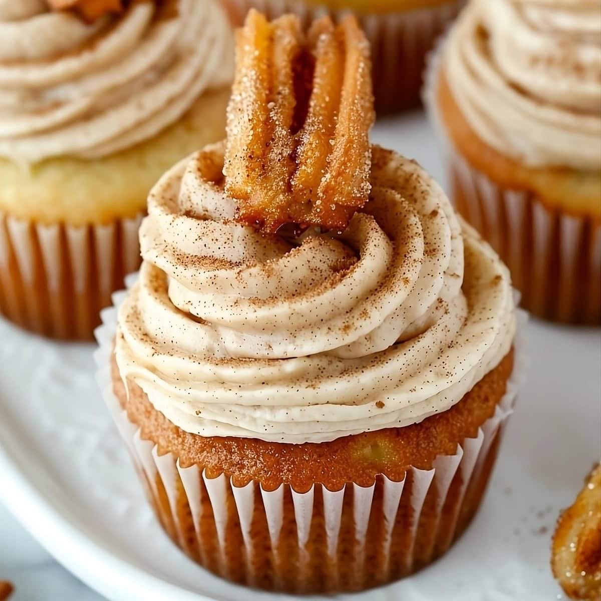 Closeup of churro cupcake on a plate with cinnamon frosting and piece of churro as garnish.