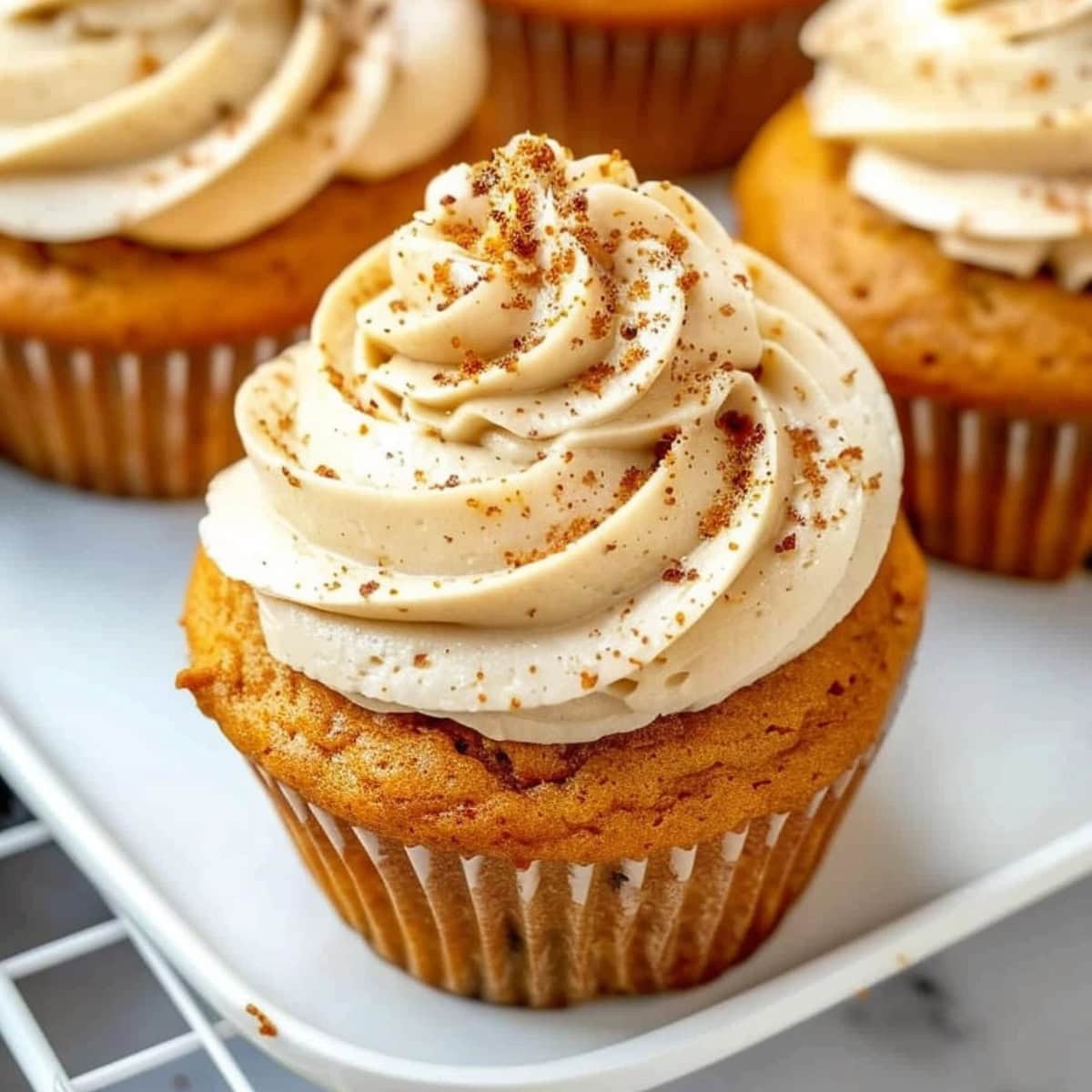 Pumpkin cupcakes on a white tray topped with cream cheese frosting.