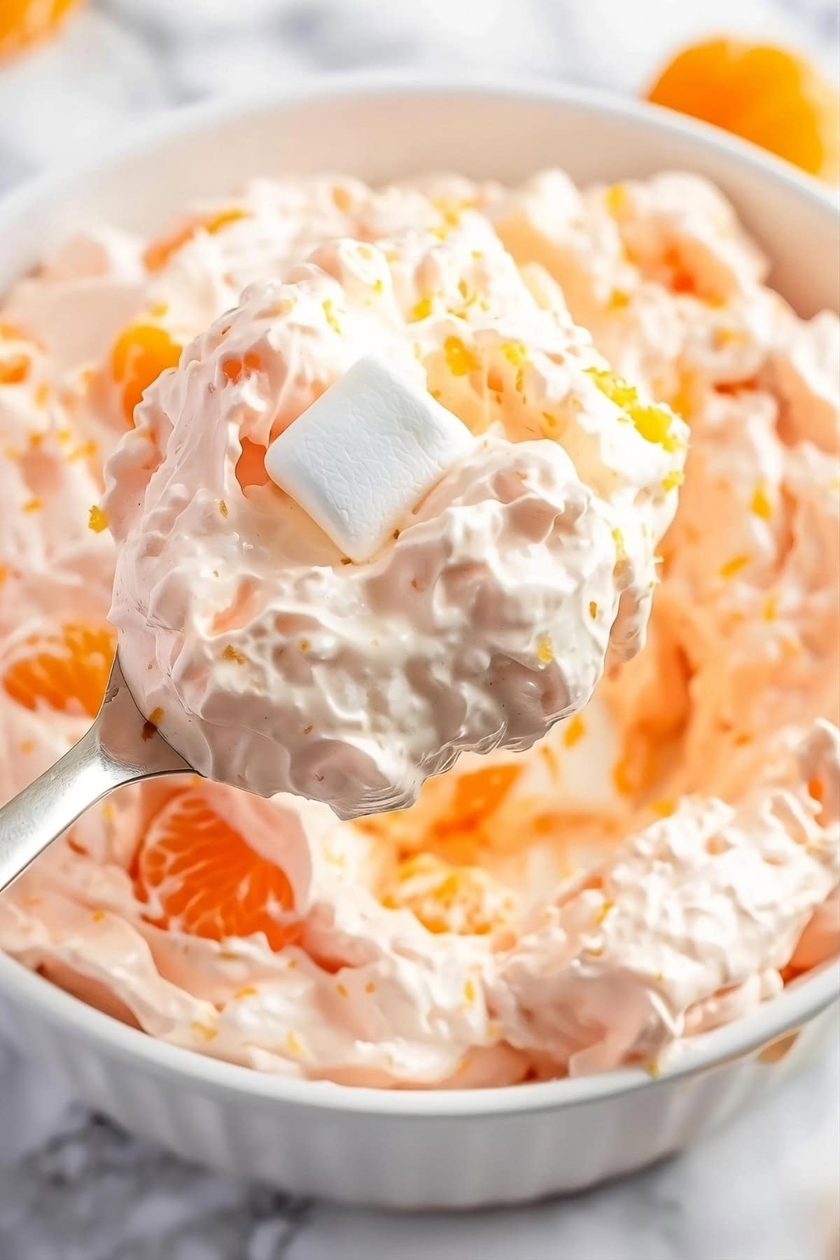 Closeup of spoonful of orange fluff salad from a white bowl.