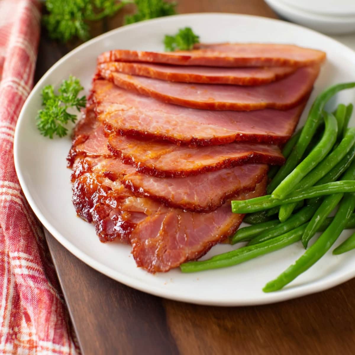 Coca-cola glazed ham with green beans in a white plate.