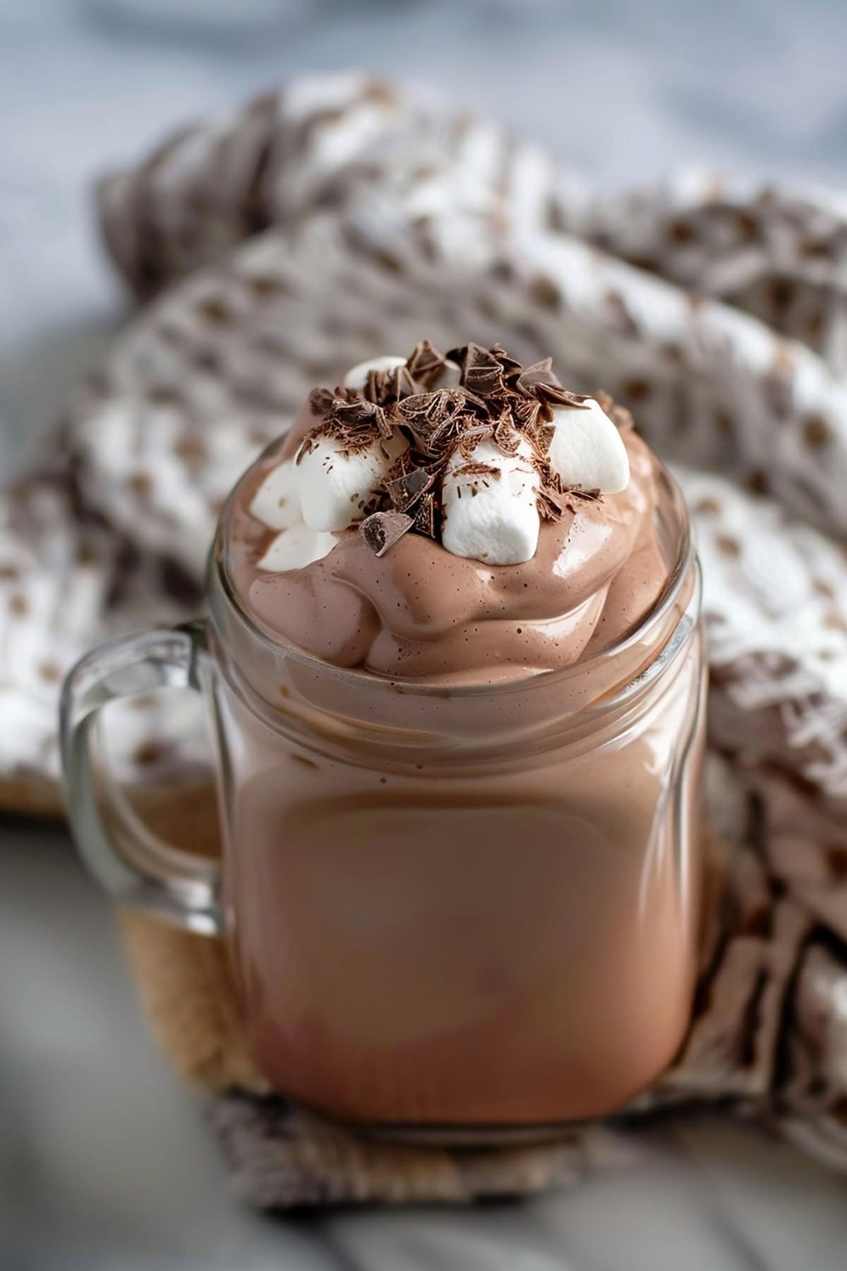 Creamy whipped hot chocolate in a mug glass topped with mini marshmallows and chocolate shavings
