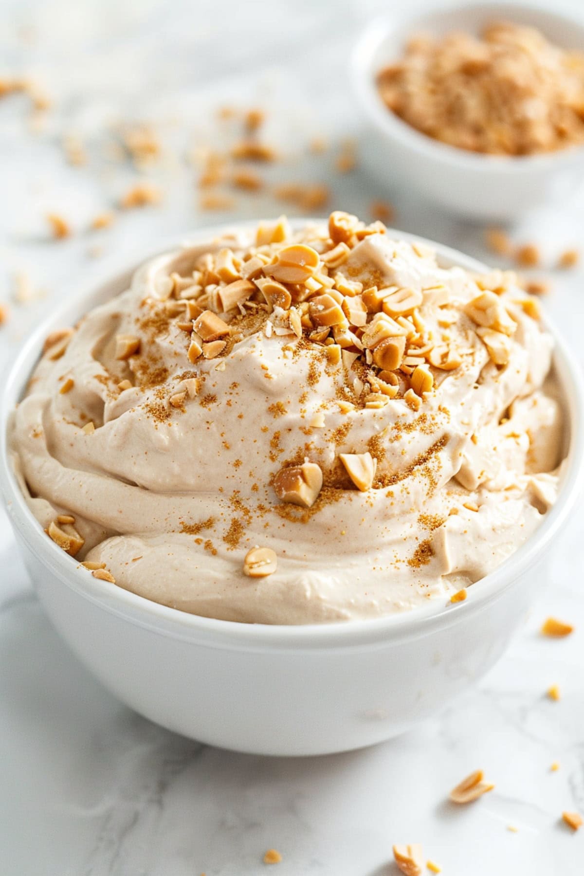 White bowl with peanut butter dip with crushed peanuts on top.