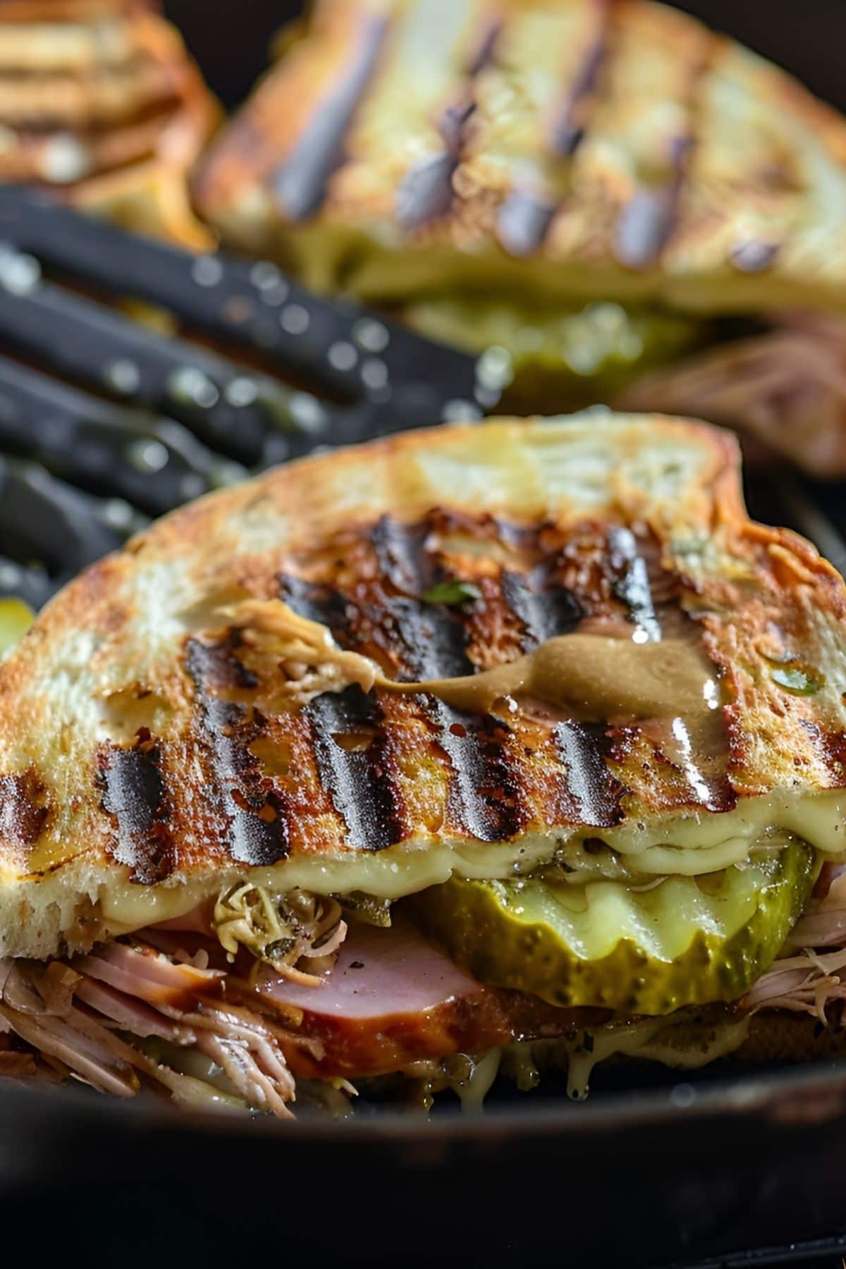 Grilled Cuban Sandwich Paninis with Pork, Ham, Mustard, Cheese, and Pickles in the Pan with a Spatula Close UP