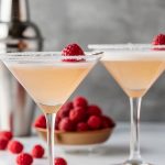 Two French Martinis in Two Sugar-Rimmed Martini Glasses with Fresh Raspberries for Garnish with a Cocktail Shaker and Bowl of Raspberries in the Background