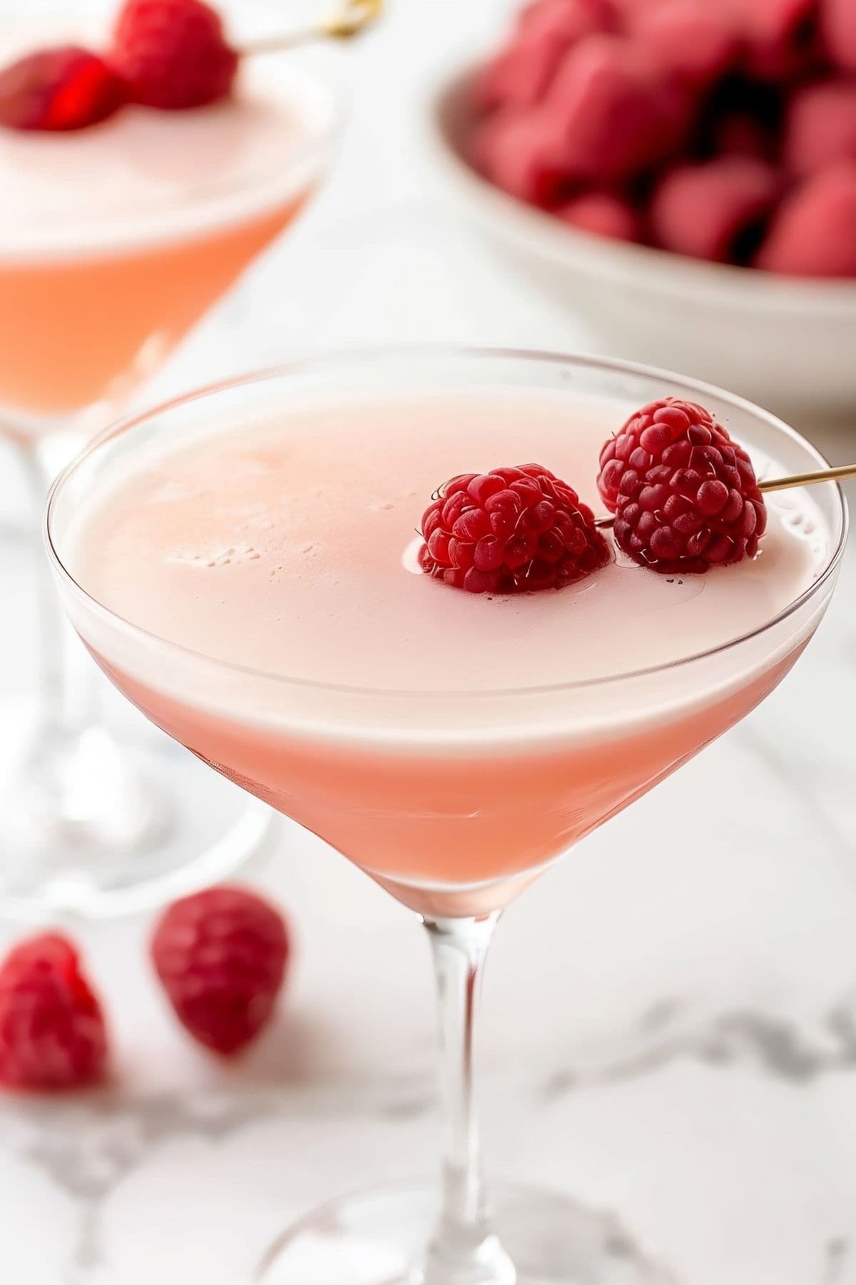 Close Up of French Martini with Fresh Raspberries, a Second Martini and a Bowl of Raspberries in the Background