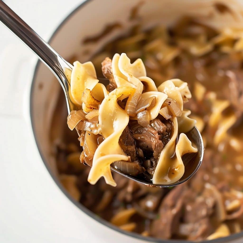 Creamy bite-sized beef, noodles and onions in a spoon, close-up